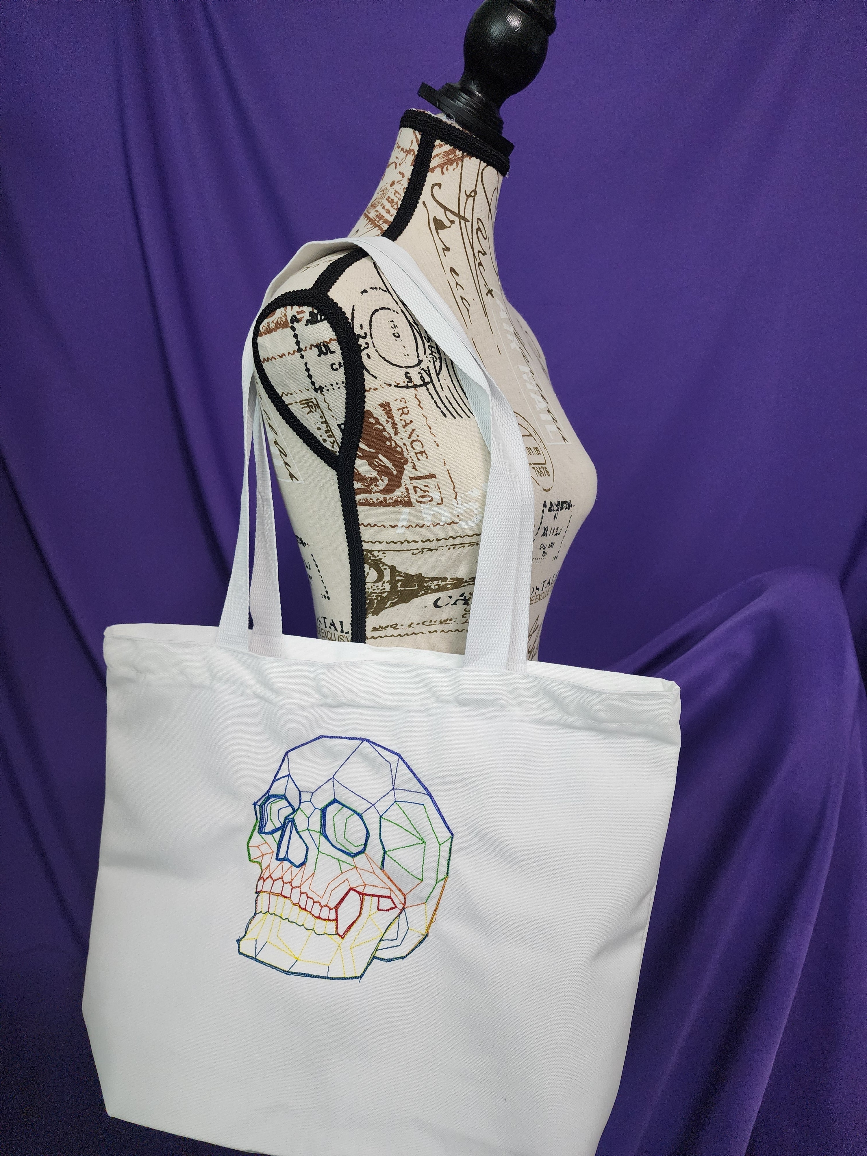 white tote bag with rainbow skull embroidery on it