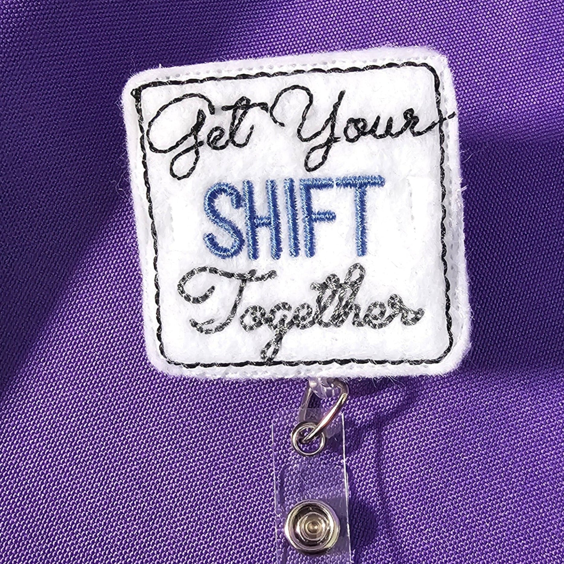 A badge reel with a square attachment featuring the text 'Get Your Shift Together' on a purple background.